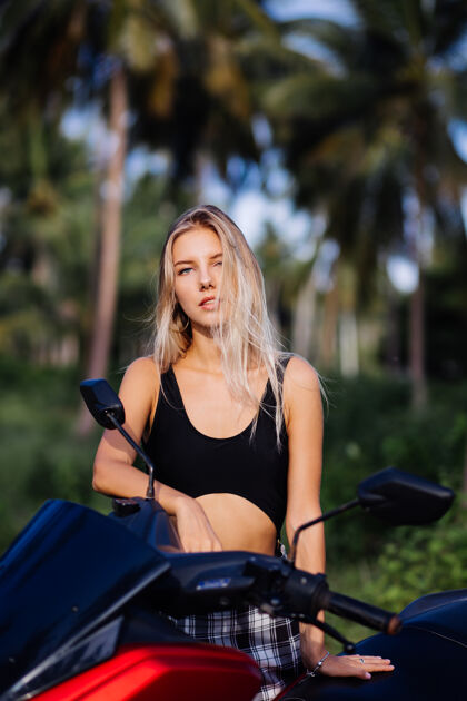 漂亮穿着黑色上衣泳衣和格子黑白裙的苗条年轻女子的肖像 骑着摩托车在热带丛林中驰骋度假年轻树