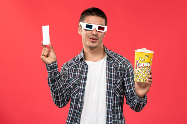 西装正面图年轻男子手持爆米花和票在红墙电影院的d太阳镜肖像男人剧院