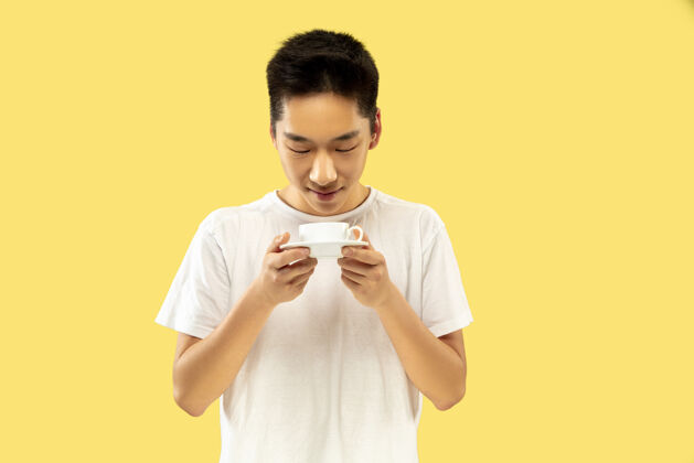 肖像韩国年轻人的肖像穿白衬衫的男模喝咖啡 感觉快乐人类情感的概念 面部表情前视流行的颜色观点模特微笑
