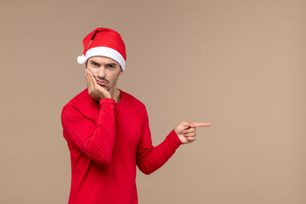 节日正面图棕色背景上困惑的年轻男子情绪圣诞假期男性帽子工作