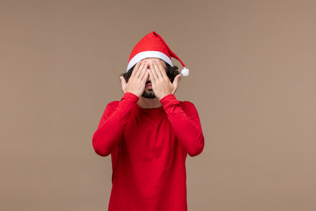 观点正面图：一个年轻人在圣诞节的棕色背景下捂着脸背景情感前面