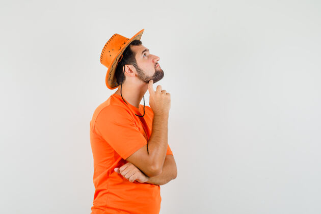 现代年轻人穿着橘色t恤 头戴帽子 神情若有所思 俯瞰前方表情工作室衬衫