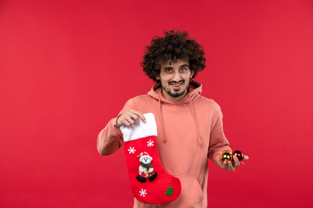 年轻一个年轻人微笑着在红墙上的圣诞玩具的正面视图身体摆姿势男性