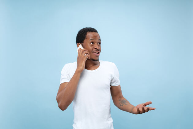肖像一个穿着白衬衫的非洲裔美国年轻人的特写照片…拿着智能手机打电话长相说话成人