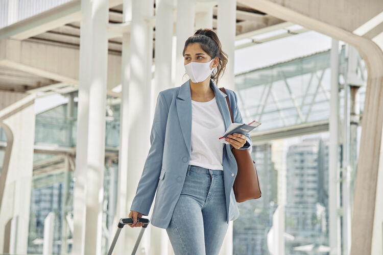 大流行大流行期间带着行李和医用口罩在机场的女人口罩冠状病毒旅行