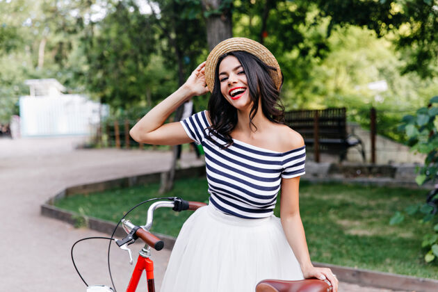自行车可爱的白种女孩戴着帽子在大自然中摆姿势漂亮的黑发女人穿着裙子 骑着自行车站在街上成人年轻欢笑