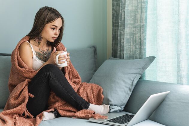 家庭大流行期间 穿着毛毯在家喝咖啡 在笔记本电脑上工作的女人流行笔记本电脑防护