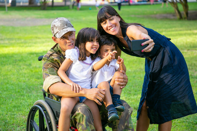 孩子快乐的残疾退役军人抱着孩子 而他的妻子在手机上自拍家庭退伍军人或回家的概念自拍手机受伤