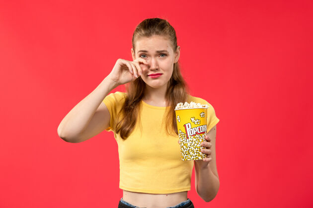 电影正面图年轻女子在电影院拿着爆米花 在红墙电影院假装哭女色女性假的年轻女性