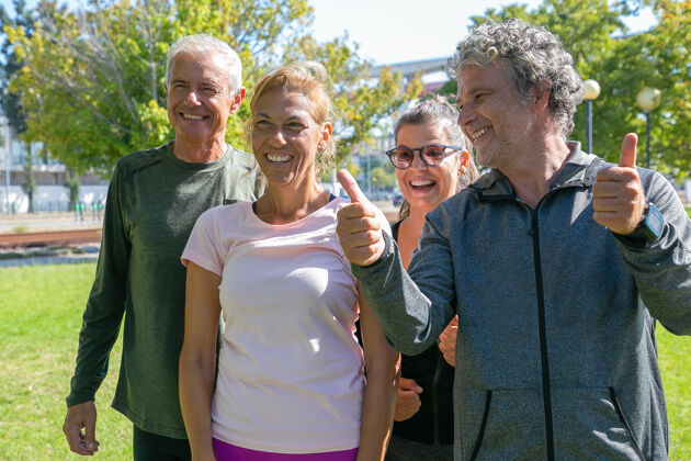跑步者快乐兴奋的运动型成熟人士在公园晨练后站在一起 面带微笑 做着竖起大拇指的手势退休或积极的生活方式概念灰色向上成熟
