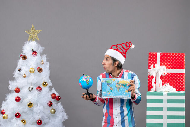 微笑正面图是一个戴着圣诞帽的男人拿着世界地图和地球仪圣诞节抱着家伙