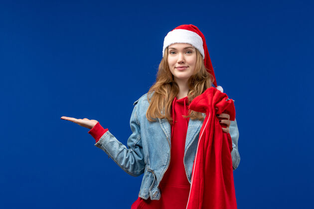 漂亮正面图：蓝色书桌上的年轻女性拿着带礼物的包 圣诞节的心情节日前面表演者
