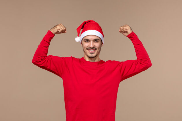 人正面图：年轻的男性微笑着 在圣诞节假期的棕色背景上弯曲成人英俊帽子