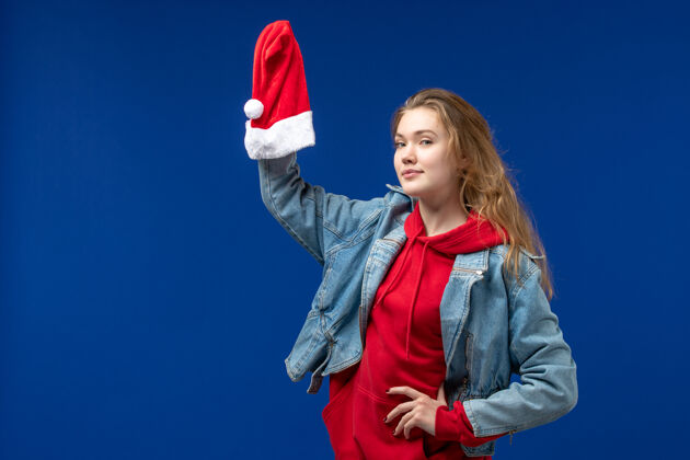 男性前视图年轻女性手持蓝色背景上的红色圣诞帽感慨圣诞色情感人商业