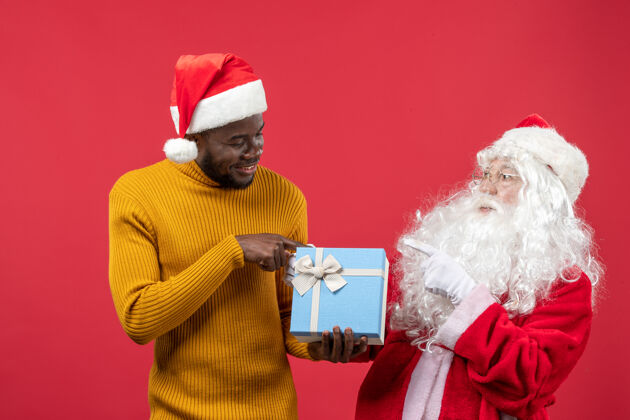 圣诞老人红墙上的圣诞老人和拿着礼物的年轻人的正视图圣诞快乐男性人