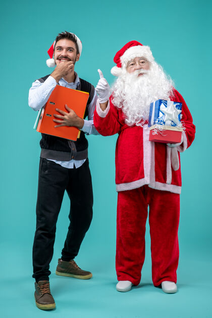 成人圣诞老人与年轻人和节日礼物在蓝色墙上的正面视图圣诞老人前面男孩