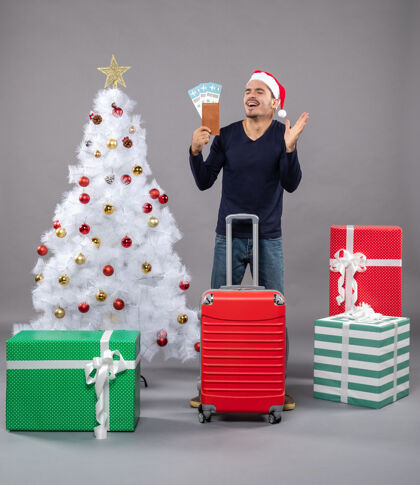 商店带着红色手提箱的笑脸男人展示着他的旅行票和灰色的击掌礼物圣诞帽圣诞老人