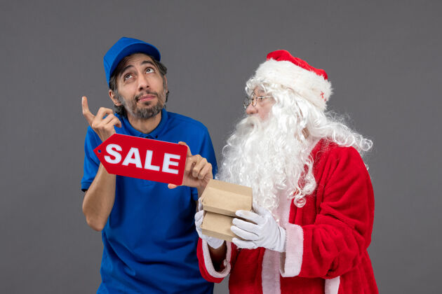 服装圣诞老人的正面图 男性信使手持销售横幅 灰色墙上有食品包装食品节日男