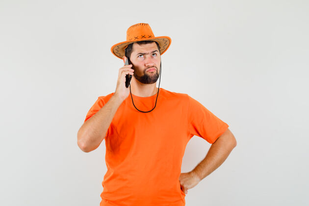成人年轻人穿着橘色t恤 戴着帽子 神情犹豫不决 正对着手机说话人衬衫男人
