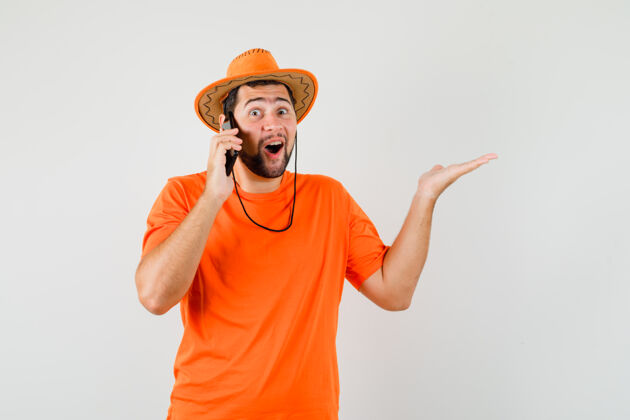 手势年轻人穿着橙色t恤 戴着帽子 正在讲手机 看上去很开心正面图衬衫模特人
