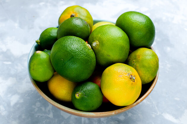 可食用前视图浅白色桌子上的酸味鲜橘和柠檬柑橘异国情调的热带水果维生素酸味柑橘办公桌新鲜