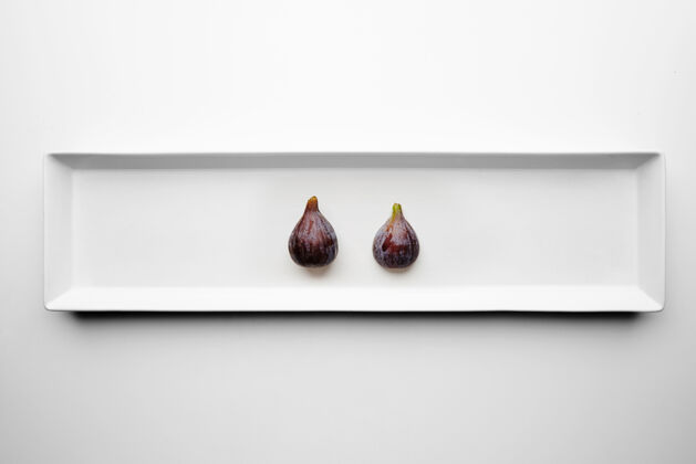 有机两个无花果孤立在中心矩形陶瓷板上的白色桌子水果细节多汁