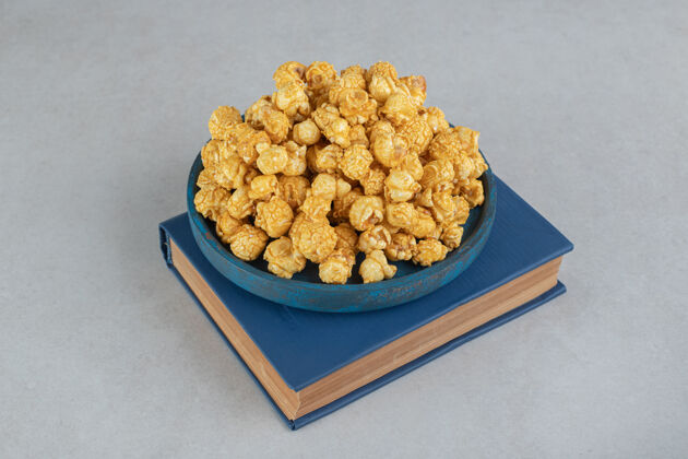 托盘一小盘涂了焦糖的爆米花放在一本书的大理石上焦糖爆米花垃圾食品