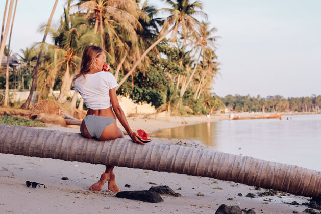 休息日落时分 在热带海滩上 一个年轻的女人拿着西瓜饮食西瓜美丽