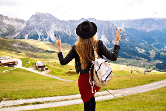 远足者美丽时尚的女人摆着姿势 仰望着令人叹为观止的山景 令人惊叹的旅行体验形象白云石全景帽子