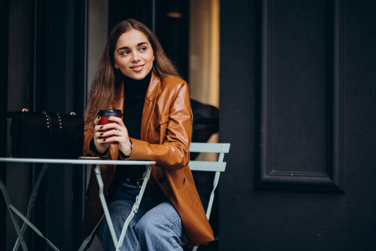 女人坐在咖啡馆外面喝咖啡的年轻女孩服装现代性感