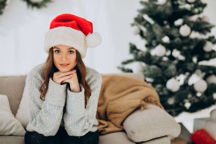 优雅坐在圣诞树旁沙发上的年轻女子传统快乐圣诞盒