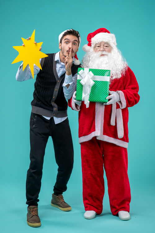 抱着前视图：圣诞老人和手持蓝色背景黄色标志的年轻男性圣诞老人圣诞老人年轻