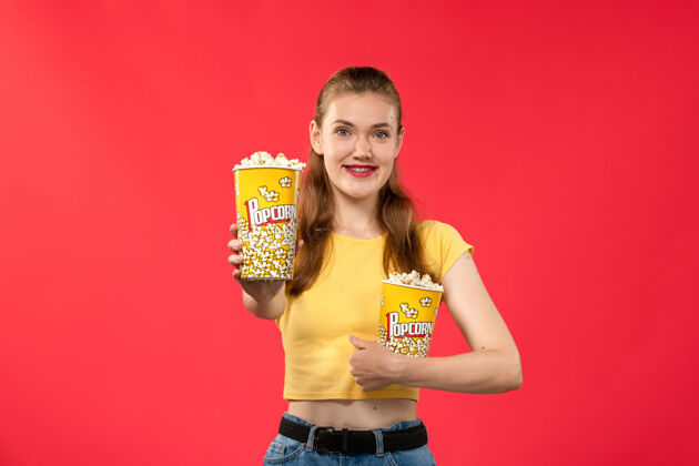 年轻人正面图年轻女性在电影院拿着爆米花包在浅红墙电影院看女性趣味电影剧院年轻的女性电影院