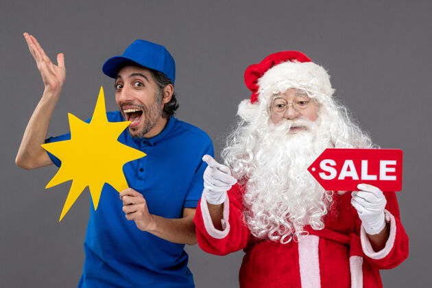 人圣诞老人的正面图 男信使举着销售横幅 灰色墙上挂着黄色的牌子男人庆祝圣诞快乐