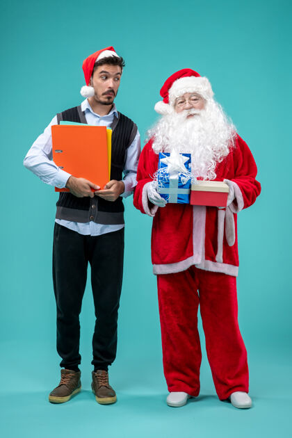 十二月圣诞老人与年轻男性和礼物在蓝色墙上的正面视图庆祝假期快乐