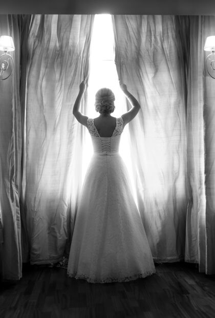 室内黑白后视图优雅的新娘在卧室的大窗户摆姿势背光女士卧室