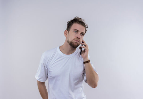 男人穿着白色t恤的悲伤的年轻人在孤立的白色背景下讲电话T恤穿着悲伤