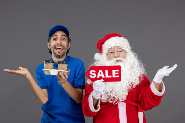 咖啡圣诞老人的正面图 男信使拿着售货笔 灰色墙上挂着咖啡举行庆祝圣诞老人