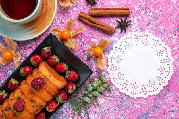 茶俯瞰美味的蛋糕 放在黑色的蛋糕锅里 粉红色的桌子上放着新鲜的红色草莓和茶托盘烘焙饼干