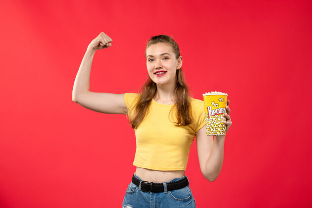 女性正面图年轻的女性在电影院拿着爆米花包和红墙电影影院小吃女趣味电影电影包装小吃