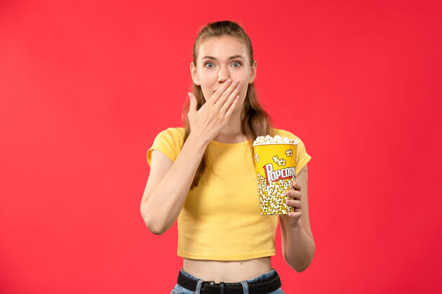 剧院正面图年轻女子在电影院拿着爆米花在浅红的墙上电影院女彩色成人视图女性
