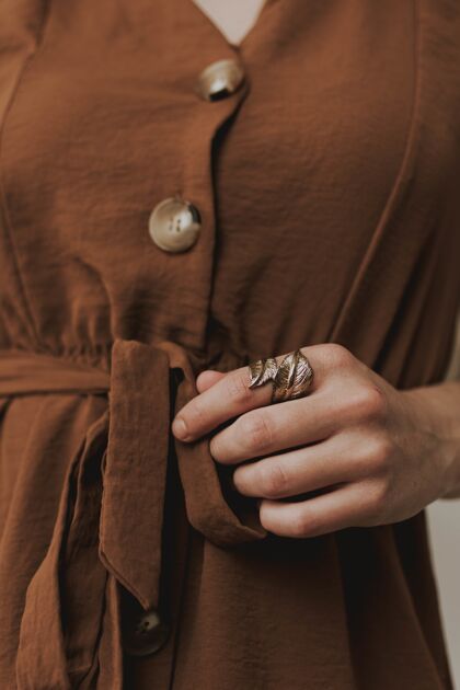优雅垂直特写镜头中的一位女性身穿棕色连衣裙 戴着一枚金属叶形戒指时尚可爱金属