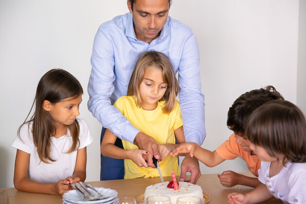 用餐可爱的小女孩在爸爸的帮助下切生日蛋糕快乐可爱的孩子们一起庆祝生日 在餐厅等待甜点童年 庆祝和节日的概念孩子白种人女儿