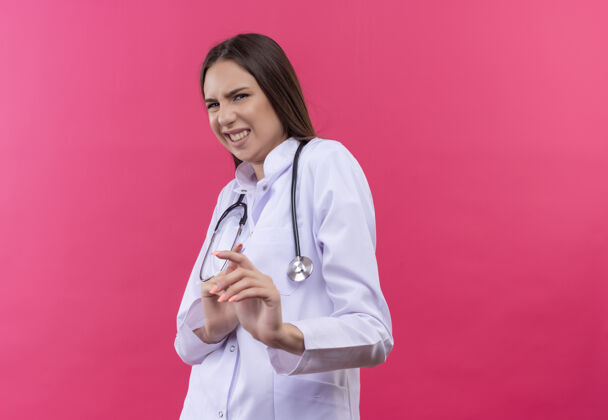 医疗穿着听诊器医用长袍的神经质的年轻女医生 背景是孤立的粉色医生穿着听诊器