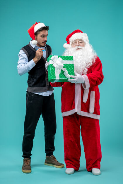 前面圣诞老人与年轻人和节日礼物在蓝色墙上的正面视图成人圣诞老人圣诞老人