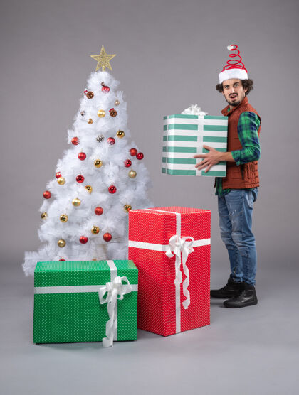 购物年轻的男性在灰色的圣诞礼物周围圣诞树年轻年轻男性