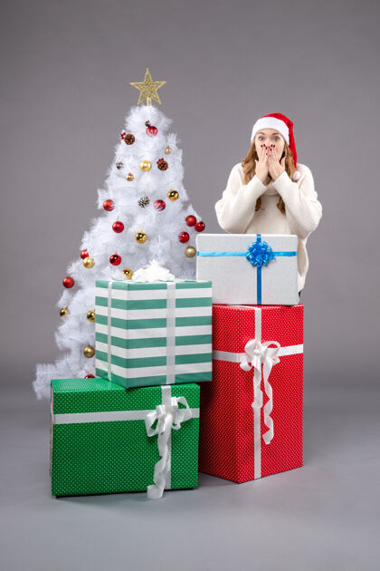 购物年轻的女性在灰色的圣诞礼物周围圣诞树圣诞帽帽子