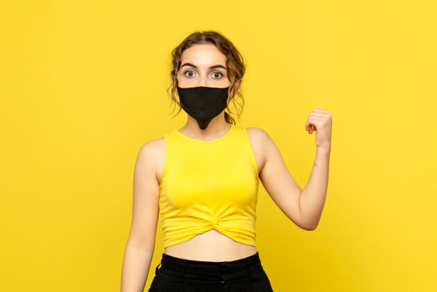 年轻女性黄墙上戴着黑面具的年轻女子的正视图流行人漂亮