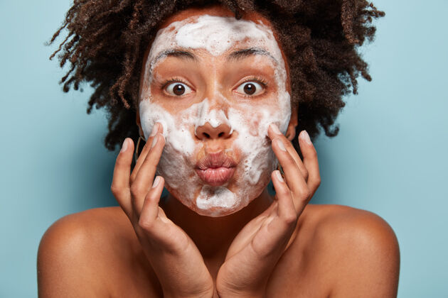 年轻人 健康 卫生和皮肤问题的概念可爱的非洲裔美国女士保持嘴唇折叠 触摸脸颊 有白色泡沫的脸上 用美容凝胶清洗 感觉清新 睁大眼睛洁面乳清洁头巾