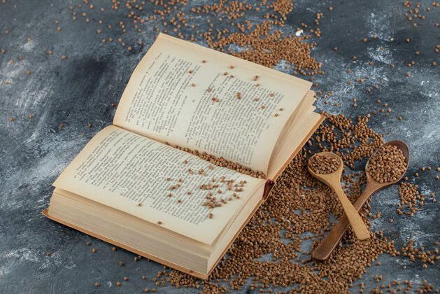 生的装满生荞麦和书的木勺放在大理石表面荞麦有机勺子